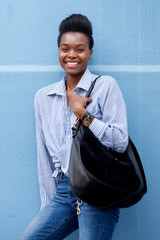 Fototapeta premium african american woman smiling with handbag against blue wall