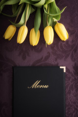 Fresh yellow tulips and menu on violet table-cloth