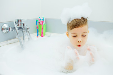 Happy young boy taking a bath. Child washes in the foam.