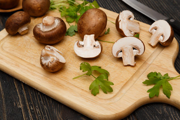 Cutted royal raw champignons with green on wooden board.