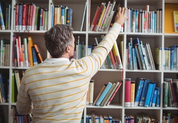Rear view of school teacher selecting book in library