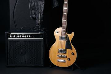 Electric bass guitar black hard case, leather biker jacket and classic amplifier on a dark background