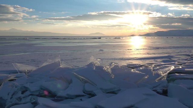 Sunset rays over small icebergs and icicles in the frozen lake