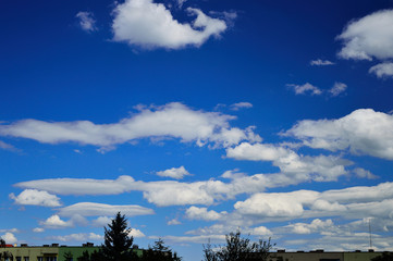 Obraz premium Chmury na błękitnym niebie nad budynkami mieszkalnymi.