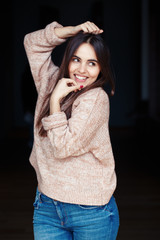 Portrait of smiling laughing white Caucasian brunette young beautiful girl woman model with long dark hair and brown eyes in turtleneck sweater and blue jeans indoor on black background