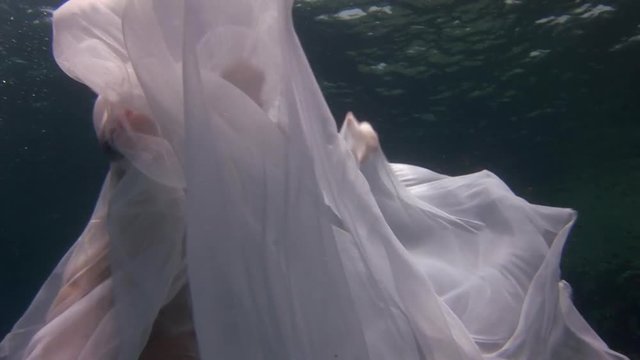 Underwater model young girl free diver in white transparent veil in Red Sea. Filming a movie at camera. Extreme sport in marine landscape, coral reefs, ocean inhabitants.