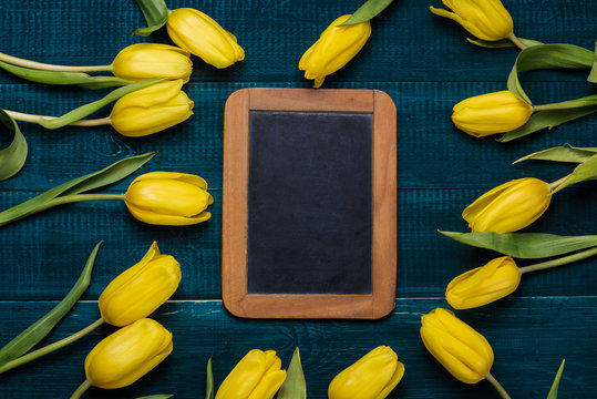 Yellow tulips on dark blue background with antique halk wooden board.