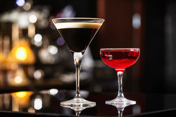 Manhattan and espresso cocktails in elegant glasses at colorful dark bar stand background.