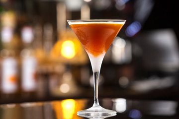 Glass of orange cocktail with vodka, syrup and wine at bar background.