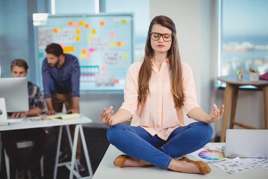 Female graphic designer sitting on table and meditating