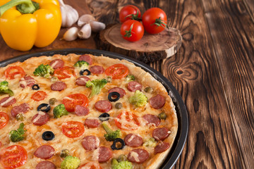 pizza with broccoli, peas, sausage, olives, peppers and tomatoes on a wooden table