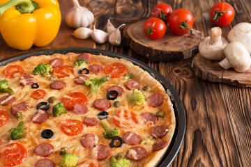 pizza with broccoli, peas, sausage, olives, peppers and tomatoes on a wooden table