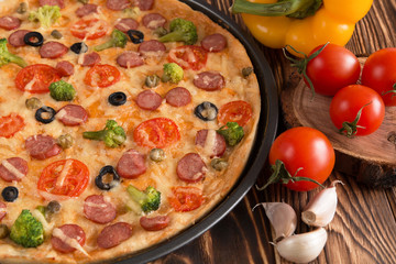 pizza with broccoli, peas, sausage, olives, peppers and tomatoes on a wooden table
