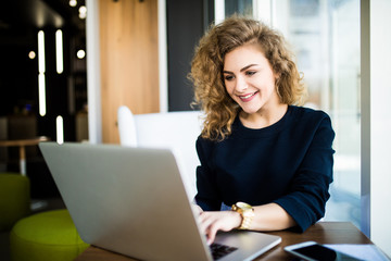 Happy curlu young woman use laptop in modern place with bright windows.