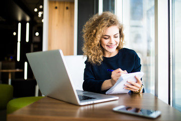 Happy curlu young woman use laptop in modern place with bright windows.