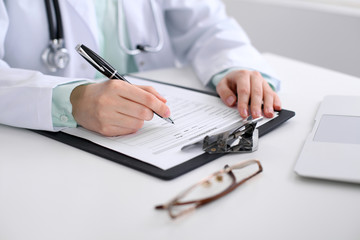 Close-up of a female doctor filling  out application form , sitting at the table in the hospital