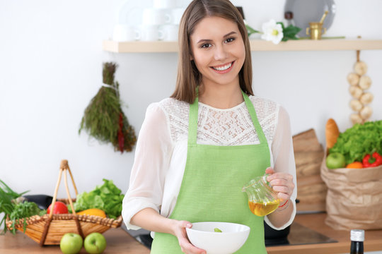 Young happy woman is cooking or eating fresh salad in the kitchen. Food and health concept