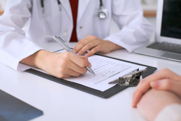 Close up of a female doctor filling up  an application form while consulting patient. Medicine and health care concept