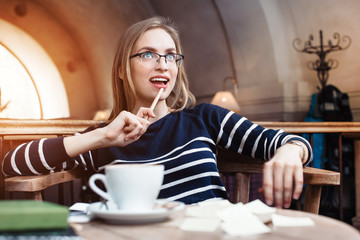 Suprised smile young woman in glasses dreams seat in a cafe with cup of coffee with wooden pencil in hand. Concept of planning personal traning schedule. Looking away.