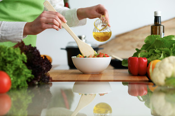 Close-up of human hands cooking vegetables salad in kitchen on the glass table with reflection. Healthy meal and vegetarian concept