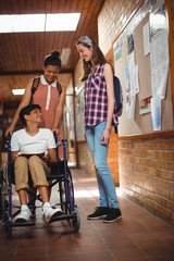 Schoolgirls talking with her disabled friend in corridor