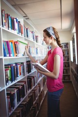 Schoolgirl selecting book from book shelf in library