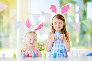 Two cute little sisters wearing bunny ears playing egg hunt on Easter