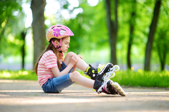 Pretty little girl learning to roller skate on beautiful summer day in a park
