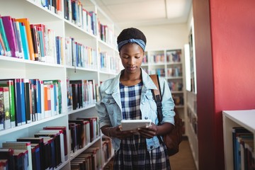 Attentive schoolgirl using digital tablet in library