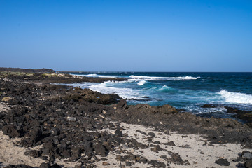 Black volcano stones and white sand on the coastline of  the Atlantic Ocean in Canarias
