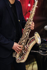 Gold saxophone with specks on it in male hands in the red background.Hands of musician playing alto...