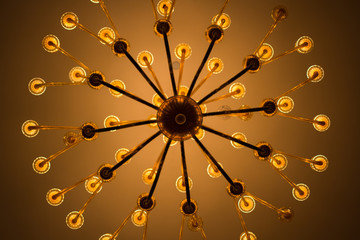 Elegant chandelier with radial arm design captured from below, warm glowing bulbs arranged in...