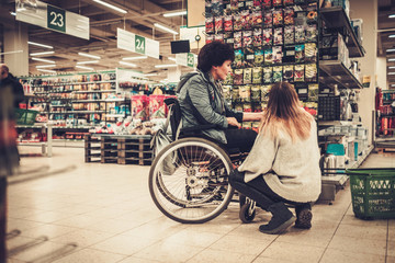 Young girl helping her disabled mothter in wheelchair in a department store