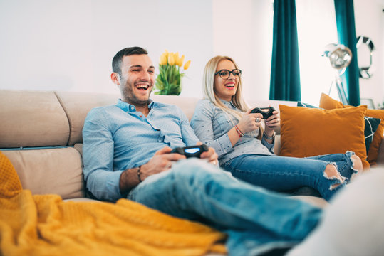 young couple having fun and laughing while playing video games in modern living room