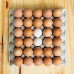 Top view of a paper egg tray filled with mostly brown eggs and a few white ones, showing natural...
