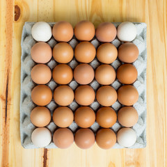 Top view of a paper egg tray filled with mostly brown eggs and a few white ones, showing natural...