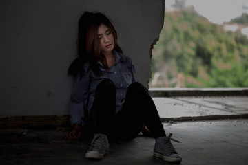 Asian woman sitting alone in an abandoned building, reflecting deep thought. A conceptual portrait...