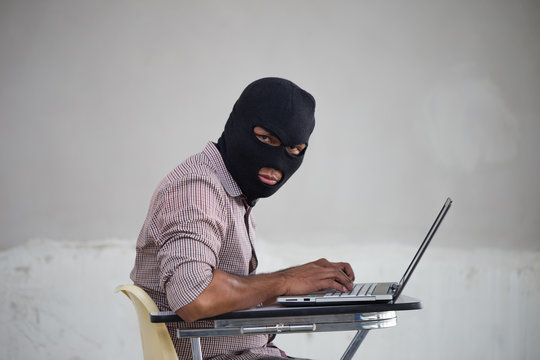 Man with weapon and mask working on a laptop, symbolizing digital security threats.