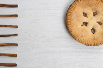 Apple pie cake lying on wooden white background with cinamon sticks