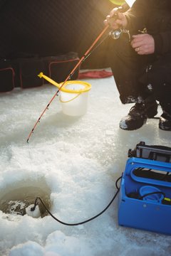 Ice fisherman sitting on chair in tent with fishing rod