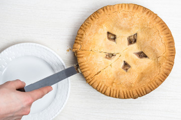 Apple pie cake lying on wooden white background with hand and knife