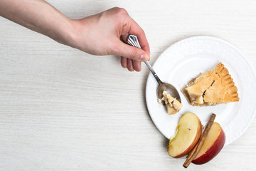 Apple pie cake lying on wooden white background with spoon in woman hand eating bite