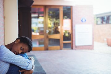 Sad schoolgirl sitting in school campus