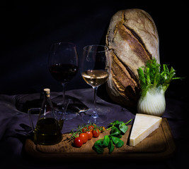 Mediterranean still life with bread, olive oil, parmesan cheese, basil, tomatoes, red and white wine