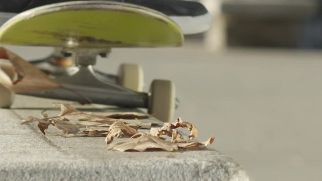 Slow motion, close up, DOF unrecognizable skateboarder jumping and sliding on concrete bench on street