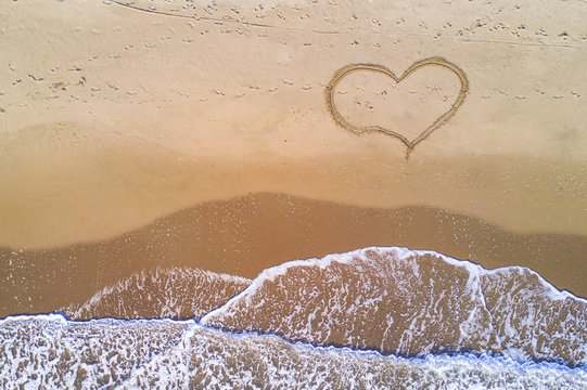 View from above, stunning aerial view of some waves crashing on a uncontaminated beach where a heart has been drawn.