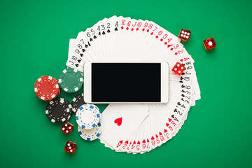 online casino concept, playing cards, dice chips and smartphone with copyspace on the green table. view from above. banner template layout mockup for online casinos and gambling.