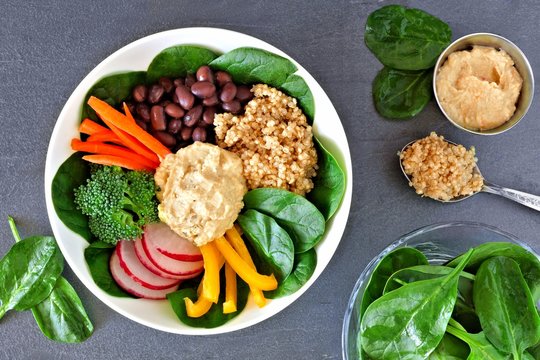 Nutritious lunch bowl with quinoa, hummus and mixed vegetables, overhead scene on a slate background
