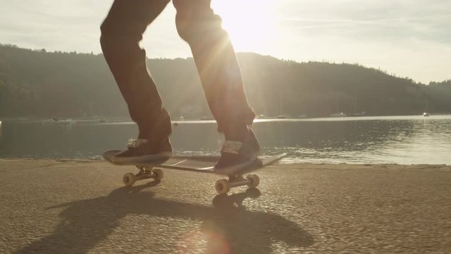 SLOW MOTION, CLOSE UP: Unrecognizable skateboarder skateboarding and jumping nollie kickflip trick on pavement along the ocean at golden light sunset. Skateboarder doing skateboard tricks by the sea