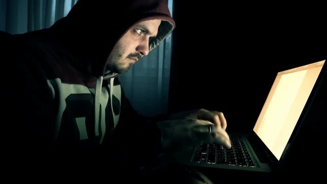 Male hacker in a hood works on a computer